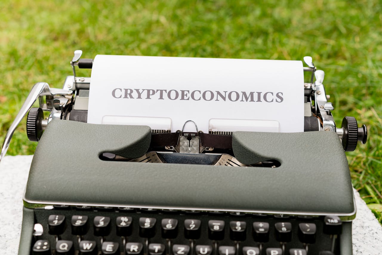 An antique typewriter with cryptoeconomics text on paper against a grassy background.