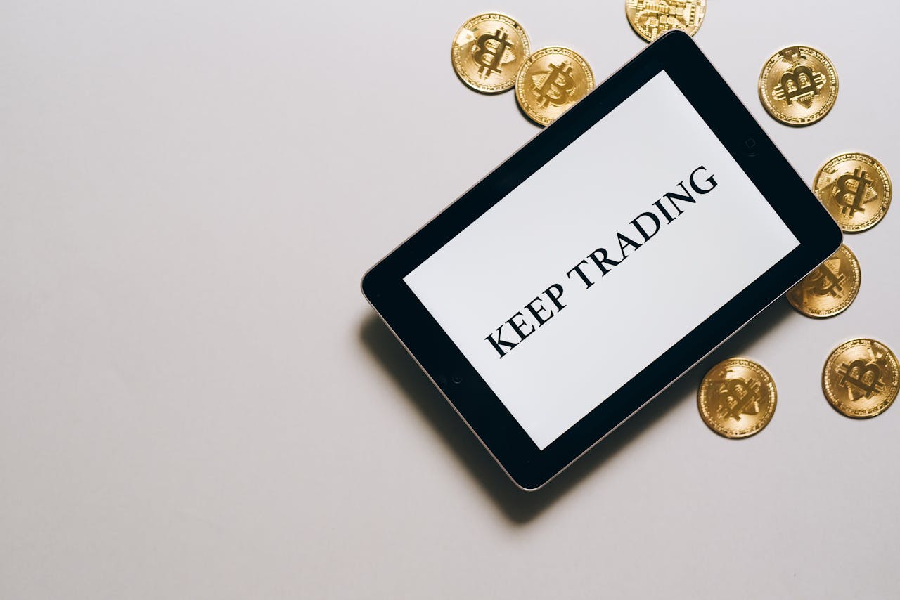 Tablet displaying 'Keep Trading' surrounded by Bitcoin coins on a white background, emphasizing digital currency and trading.